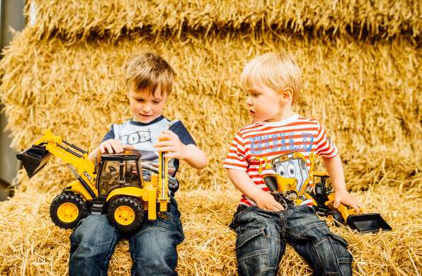Two kids sitting on a hay bale playing with JCB toys