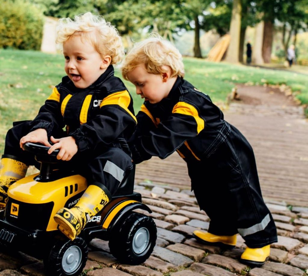 Two toddlers in JCB clothing playing with a JCB ride-on